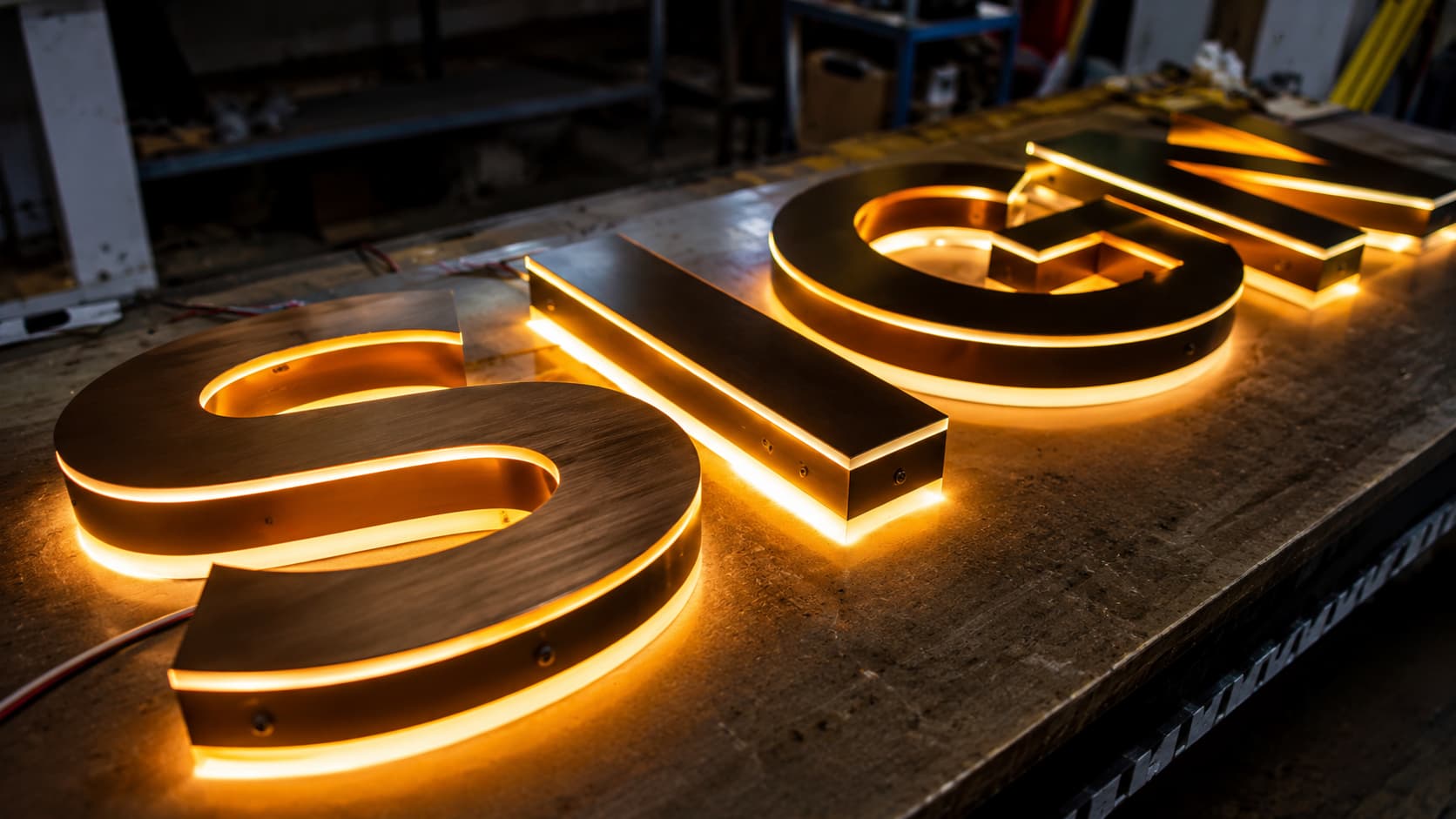 Proceso de ensamblaje de letras corpóreas doradas con iluminación cálida en el taller. Preparación de propuesta a medida para un nuevo rótulo comercial.