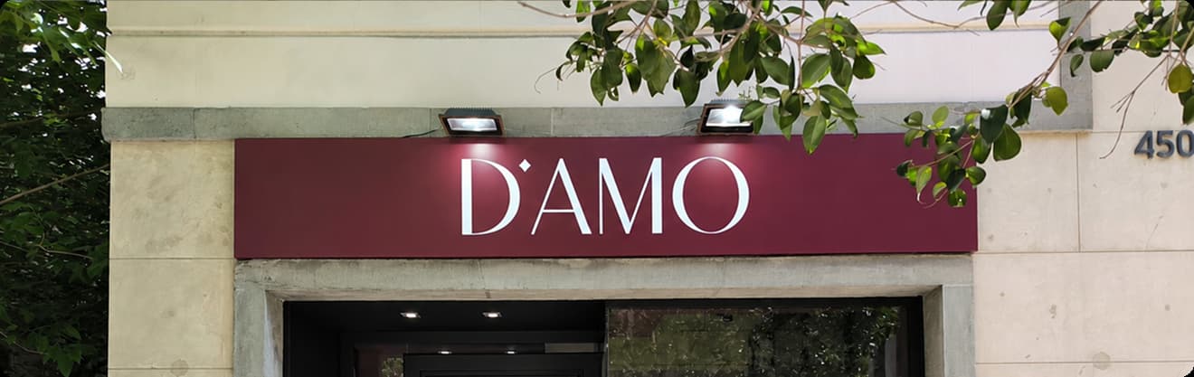 Rótulo exterior en fachada de la marca D'AMO con iluminación externa mediante focos proyectores LED